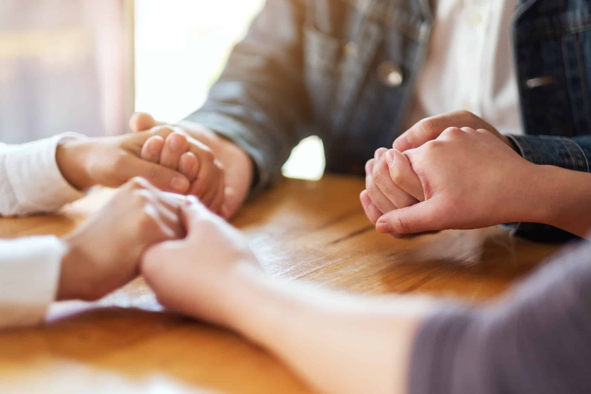 Group of people sitting in a circle holding hands and pray together or in therapy session